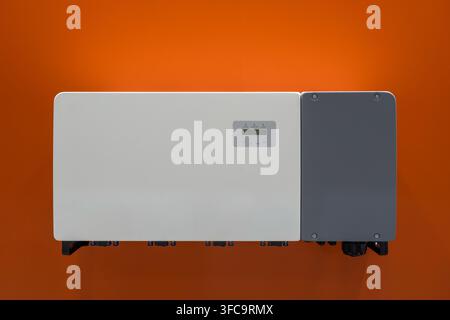 Unità ibrida di invertitore solare moderno con display di controllo montato su un muro arancione brillante per un sistema di energia rinnovabile Foto Stock