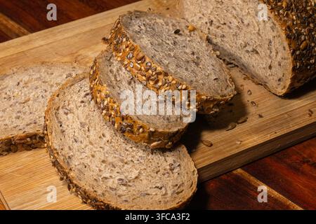 Un panino integrale appena tagliato con semi riposa su un tagliere di legno. Foto Stock