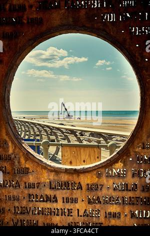 Escavatore che lavora sulla spiaggia visto attraverso l'oblò del Memoriale del Naufragio a Cleveleys, UK Foto Stock