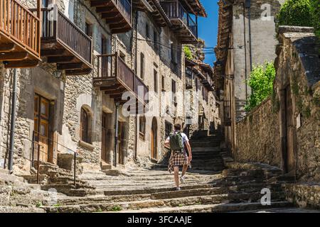 Giovane viaggiatore con zaino che sale per la strada di pietra storica del villaggio di Rupit, in Catalogna, Spagna, esplorando l'architettura medievale Foto Stock