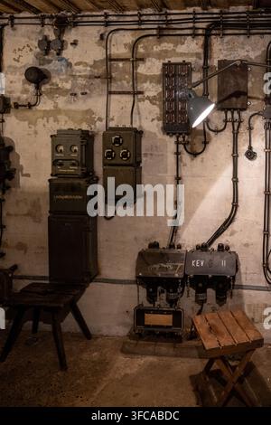 Antica apparecchiatura elettrica, cavi, scatole di controllo e lampada montati su un muro di cemento all'interno della Bessingen B-Werk in Germania. Foto Stock