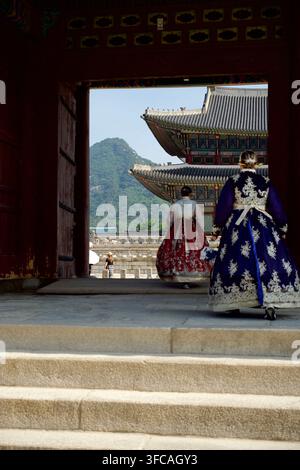 Due donne in hanbok tradizionale camminano attraverso un cancello verso una sala del palazzo coreano Foto Stock
