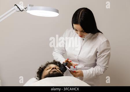 Dermatologo che utilizza un dermatoscopio per esaminare la pelle di un paziente maschio alla ricerca di nei, eseguendo un controllo di routine per il cancro della pelle Foto Stock