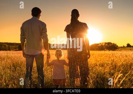 Madre e i suoi due figli seduti insieme in un campo che guardano il tramonto. Concetto di maternità e famiglia felice nella natura. Foto Stock