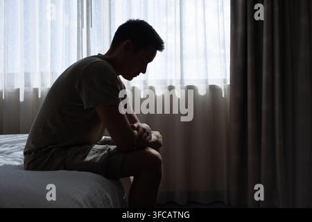 Uomo solo seduto su un letto che si sente triste. Foto Stock