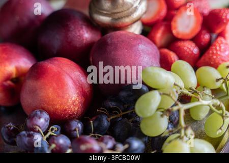 Macro di un assortimento di frutti estivi freschi multicolori, tra cui nette nectarini rossi, uva verde e nera e fragole tagliate ser Foto Stock