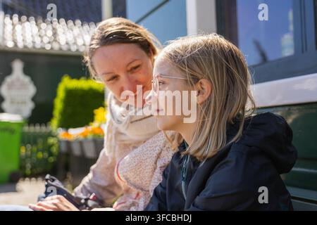 Una madre e sua figlia sono sedute insieme su una panchina mentre esplorano i Paesi Bassi. Condividono sorrisi in un vivace contesto di viaggio. Foto Stock
