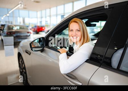 Donna seduta in una nuova auto presso un concessionario, che prende una decisione di acquisto Foto Stock
