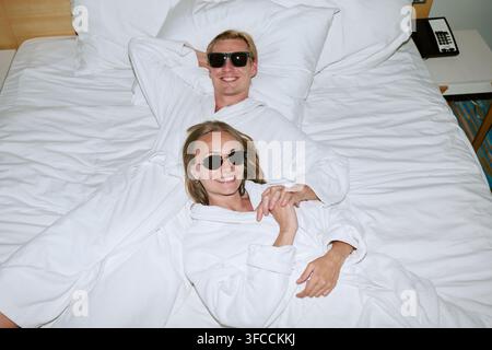 Ritratto di una coppia felice in accappatoi che si rilassa sul letto nella camera d'albergo Foto Stock