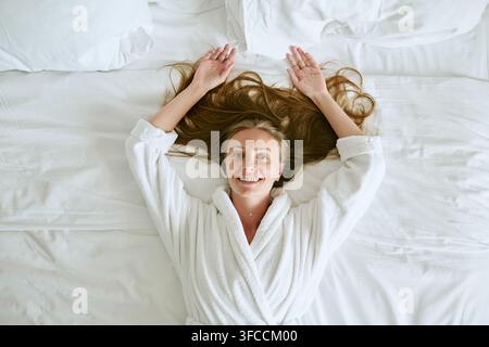 Ritratto di una donna sorridente in accappatoio sdraiata su un letto nella camera di un hotel Foto Stock