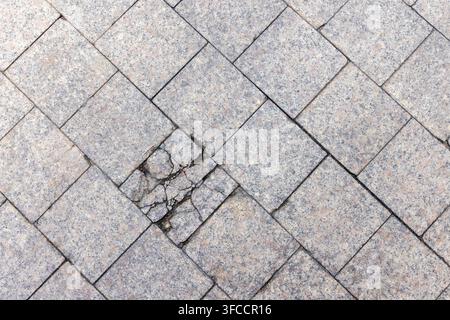 Lastricioli di granito con un blocco rotto disposti in un motivo di pavimentazione diagonale, che mostrano una superficie consumata, giunti rotti e ghiaia esposta. Adatto Foto Stock