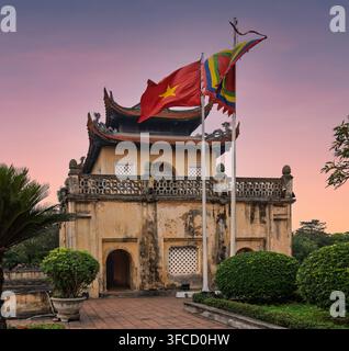 La porta storica Doan Mon alla Cittadella imperiale di Thang Long a Hanoi, Vietnam, con la bandiera nazionale e una bandiera buddista tradizionale che sventola di nuovo Foto Stock