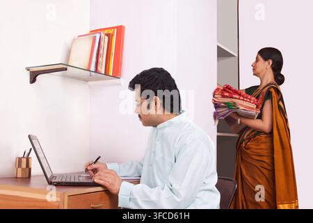 Uomo al lavoro su laptop e la donna mantenendo i vestiti in armadio Foto Stock