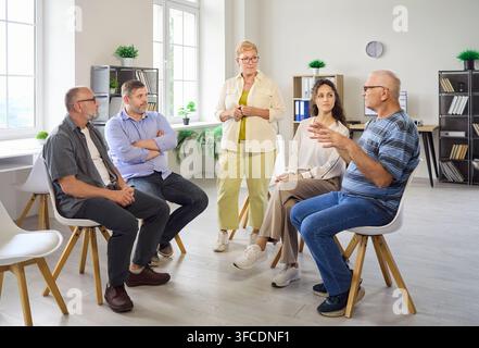 Anziani in un gruppo di supporto con un consulente che guida la discussione terapeutica Foto Stock