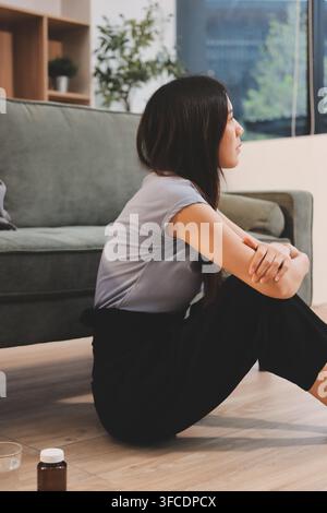 Giovane donna asiatica seduta a letto e che si tiene la testa per il dolore con mal di testa, si sente depressa e soffre Foto Stock