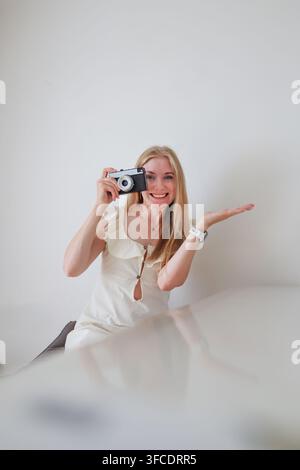 Giovane donna bionda con fotocamera compatta che sorride alla fotocamera, fotografia, creatività e concetto di narrazione visiva. Foto Stock