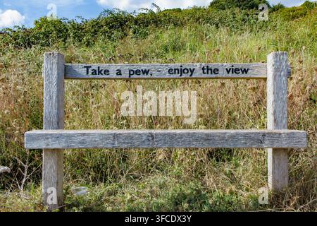 Una semplice panchina con le parole "Take a Pew, Enjoy the View" incise sulle bianche scogliere di Dover, Kent Foto Stock