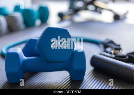 Vista ravvicinata di manubri blu da 2 kg e di una banda di resistenza disposti su un tappetino da palestra ruvido, pronti per una sessione di allenamento Foto Stock