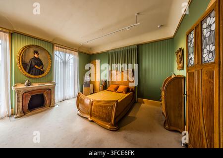 Un letto matrimoniale in legno riccamente curvato si trova in una camera da letto della Villa Majorelle a Nancy. Sopra il caminetto è appeso un ritratto ovale di una donna in abiti scuri, le pareti ricoperte da un motivo a strisce verde Art Nouveau. L'architetto Henri Sauvage costruì la casa Art Nouveau nel 1901/1902 per il designer di mobili Louis Majorelle. Foto Stock