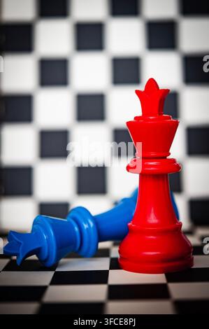 Re degli scacchi rosso in piedi mentre un re blu giace sconfitto su una scacchiera bianca e nera, simboleggiando la vittoria e la competizione Foto Stock