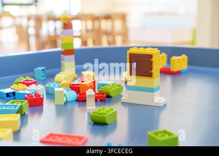 Blocchi da costruzione in plastica colorati sparsi su un tavolo da gioco blu in un'aula luminosa, concetto di educazione prescolare e gioco creativo. Foto Stock