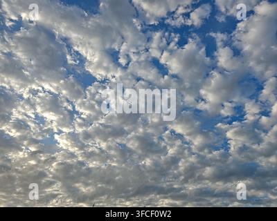 La luce del sole screziata illumina una vasta distesa di nuvole bianche strutturate che fluttuano in un cielo blu profondo, vivace e sereno. Foto Stock