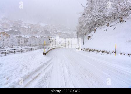 Strada vuota coperta di neve che attraversa un villaggio di montagna nelle Alpi durante una bufera di neve in inverno Foto Stock