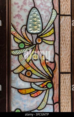 Un pannello di vetro colorato con vetro sfaccettato, dalle tonalità di gioiello e un motivo stilizzato di piante decora una porta interna al Musée de l'École de Nancy in Rue du Sergent Blandan a Nancy, Grand Est, Francia. Foto Stock