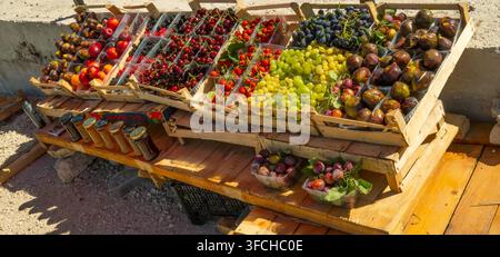 Assortimento colorato di frutti stagionali freschi disposti in casse di legno su una bancarella di mercato all'aperto lungo la strada, tra cui uva, fichi, ciliegie, fragole Foto Stock