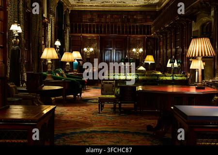 Interno della biblioteca di Chatsworth House con scaffali in legno, lampade da tavolo e arredamento classico Foto Stock