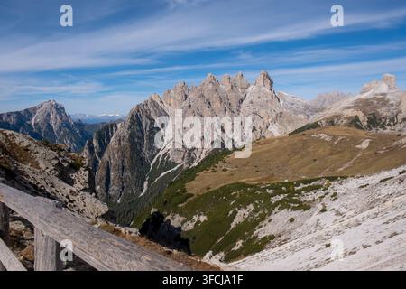 Picchi alpini frastagliati si ergono sopra valli dorate sotto cieli azzurri, ideali per viaggi, avventura e contenuti naturali. Foto Stock