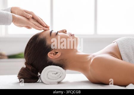 Bella donna asiatica in salone termale godere di massaggio testa di acupressure, ottenere un trattamento benessere con massaggiatore professionale, femminile rilassata sdraiata su ta Foto Stock
