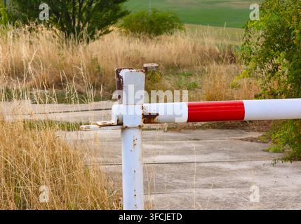 Vecchio cancello arrugginito rosso e bianco che blocca una strada in cemento Foto Stock