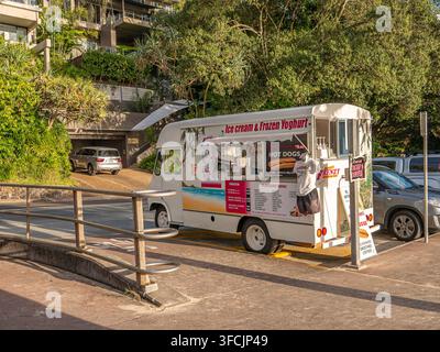 Camioncino bianco parcheggiato accanto alla strada. Il camion ha un menu colorato sul lato. Alberi ed edifici sono visibili sullo sfondo Foto Stock