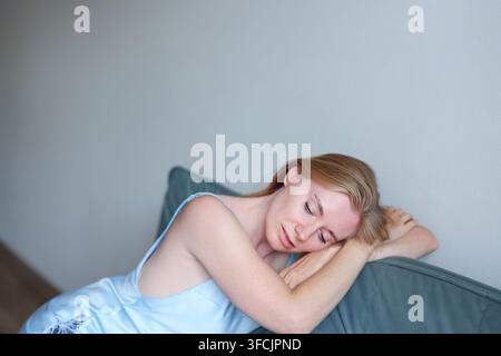 Donna bionda felice con lentiggini naturali che si rilassa in interno, umore positivo, fiducia e concetto di bellezza quotidiana. Foto Stock