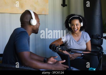 Diversi co-host che registrano un podcast vivace in un piccolo studio utilizzando cuffie bianche e micro a braccio Foto Stock