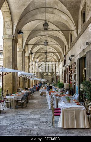 Tavoli da pranzo all'aperto sotto le arcate storiche delle Logge Vasariane in Piazza Grande, Arezzo, Toscana, Italia Foto Stock