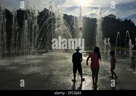 Bambini che giocano tra le fontane d'acqua in un parco in una giornata di sole Foto Stock
