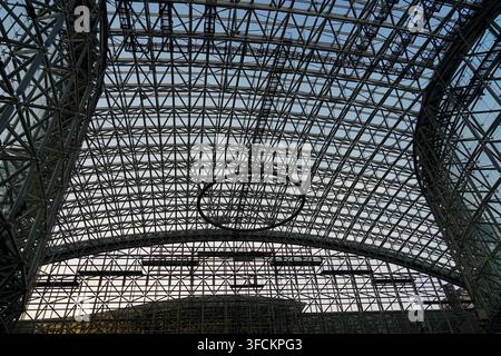 Una vista drammatica di un soffitto in vetro e acciaio di un atrio che mostra una griglia geometrica intricata e una struttura portante, evidenziando il design architettonico moderno, la simmetria, la trasparenza e l'ingegneria industriale in un interno spazioso. Foto Stock