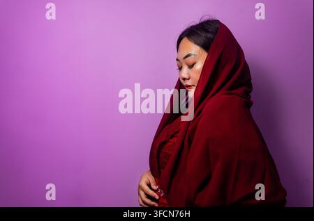 Profilo laterale di una donna sudasiatica pensierosa in hijab marrone su sfondo viola Foto Stock