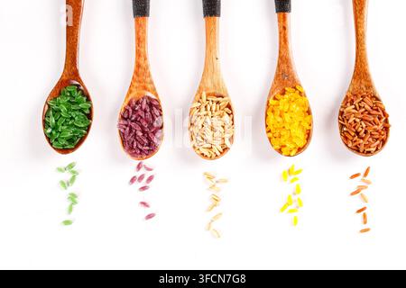 Cinque cucchiai di legno con grani di riso colorati disposti su uno sfondo bianco. Foto Stock