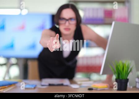 Donna d'affari risoluta indica in avanti mentre si china sulla scrivania Foto Stock