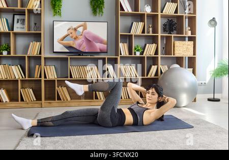 Donna che fa allenamento addominale a casa, si esercita con istruzioni di fitness sulla TV online Foto Stock