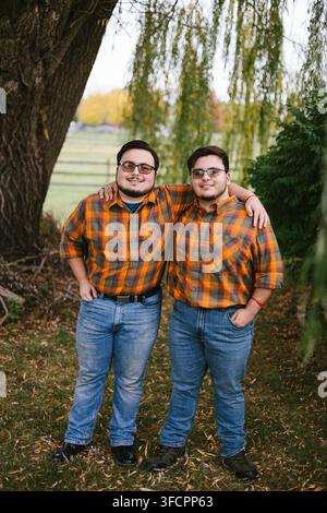 Fratelli gemelli in camicie a quadri abbinate sorridono all'aperto Foto Stock