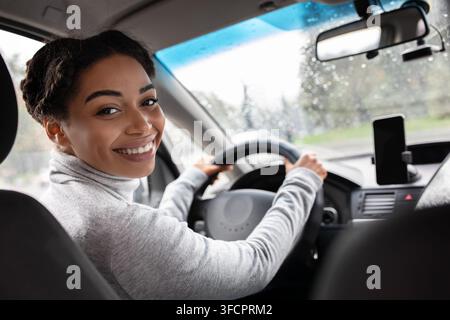 Vista posteriore della giovane donna attraente in un look casual sopra la spalla mentre guida l'automobile Foto Stock