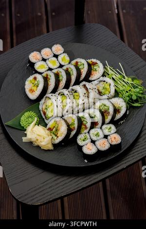 Rotoli di sushi assortiti disposti splendidamente su un piatto nero Foto Stock