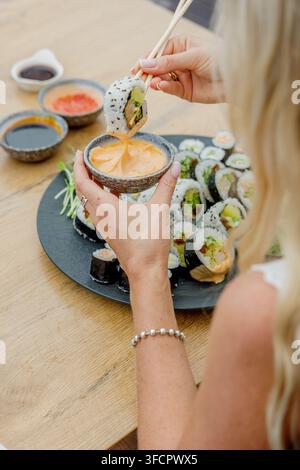 Donna che intinge un rotolo di sushi nella salsa con le bacchette Foto Stock