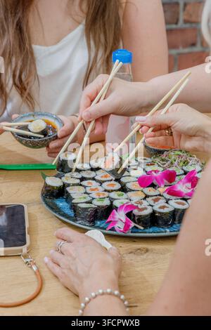 Persone che usano le bacchette per mangiare rotoli di sushi freschi Foto Stock