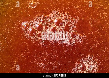 Estremo primo piano di miele di erica ambrato scuro con accumuli di piccole bolle d'aria che creano una ricca trama naturale del cibo e uno sfondo astratto. Foto Stock
