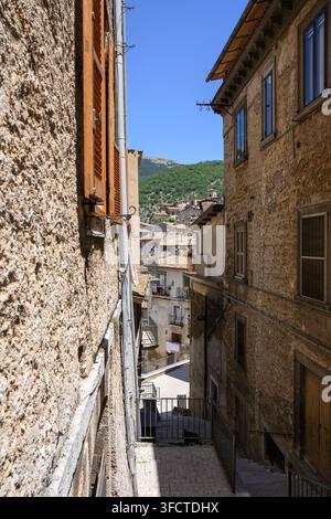 Stretta via acciottolata nella storica città di Scanno Abruzzo Italia che mostra edifici in pietra invecchiati con persiane in legno e una vista sulle case collinari Foto Stock